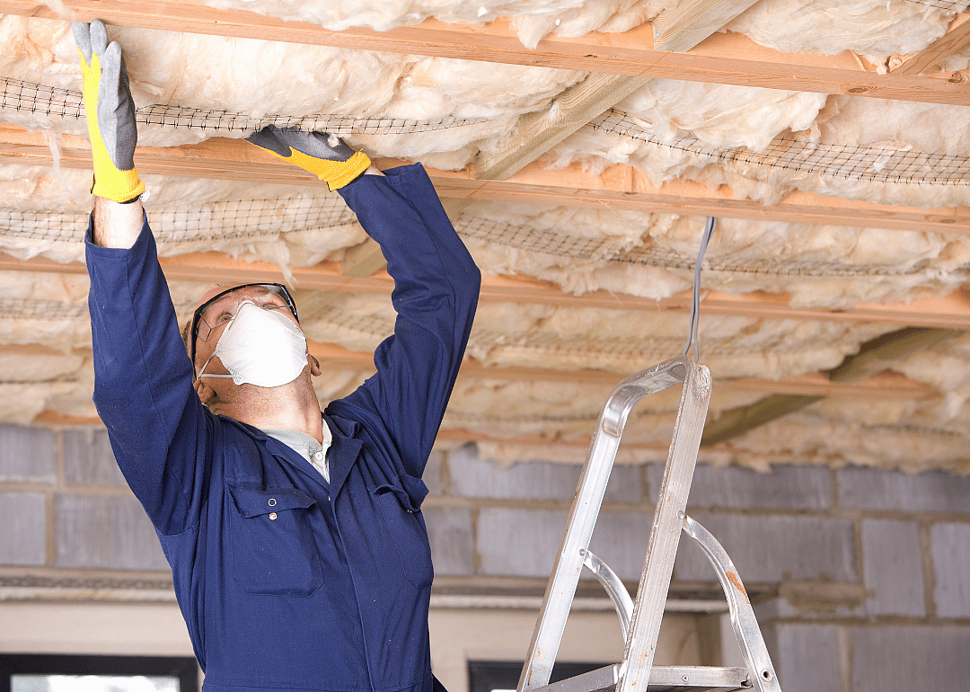 A worker in a protective mask and gloves who is installing ceiling insulation.