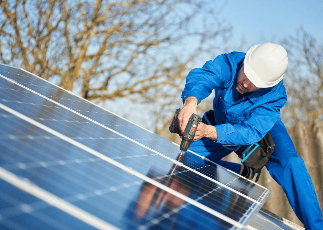 An engineer in a blue suit and protective helmet installing a stand-alone solar photovoltaic panel system