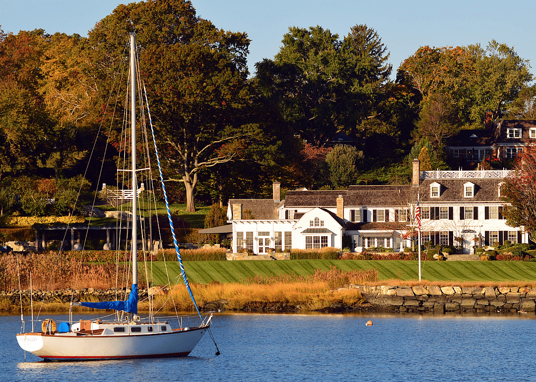 A sailboat just off shore of a luxury waterfront home in Greenwich.