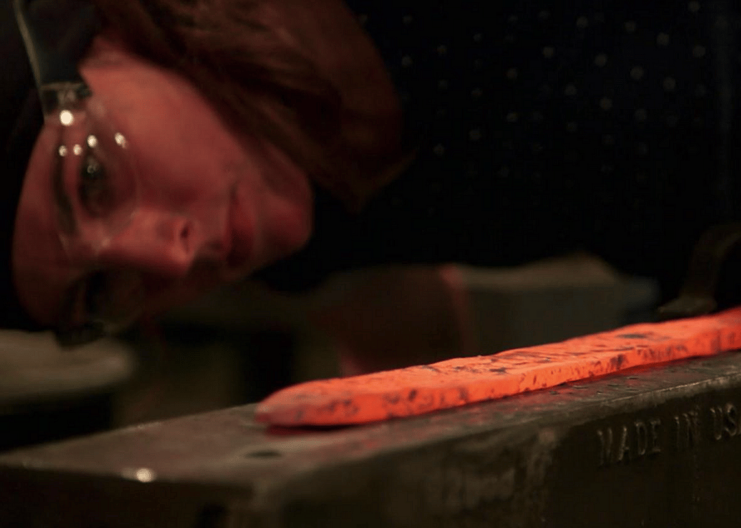 A woman watches a sword she is forging closely