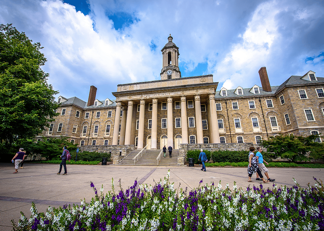 Students and adults walking in front of the Old Main building on the campus of Penn State.