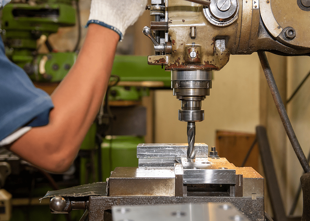 Workers bore a hole in a metal piece.