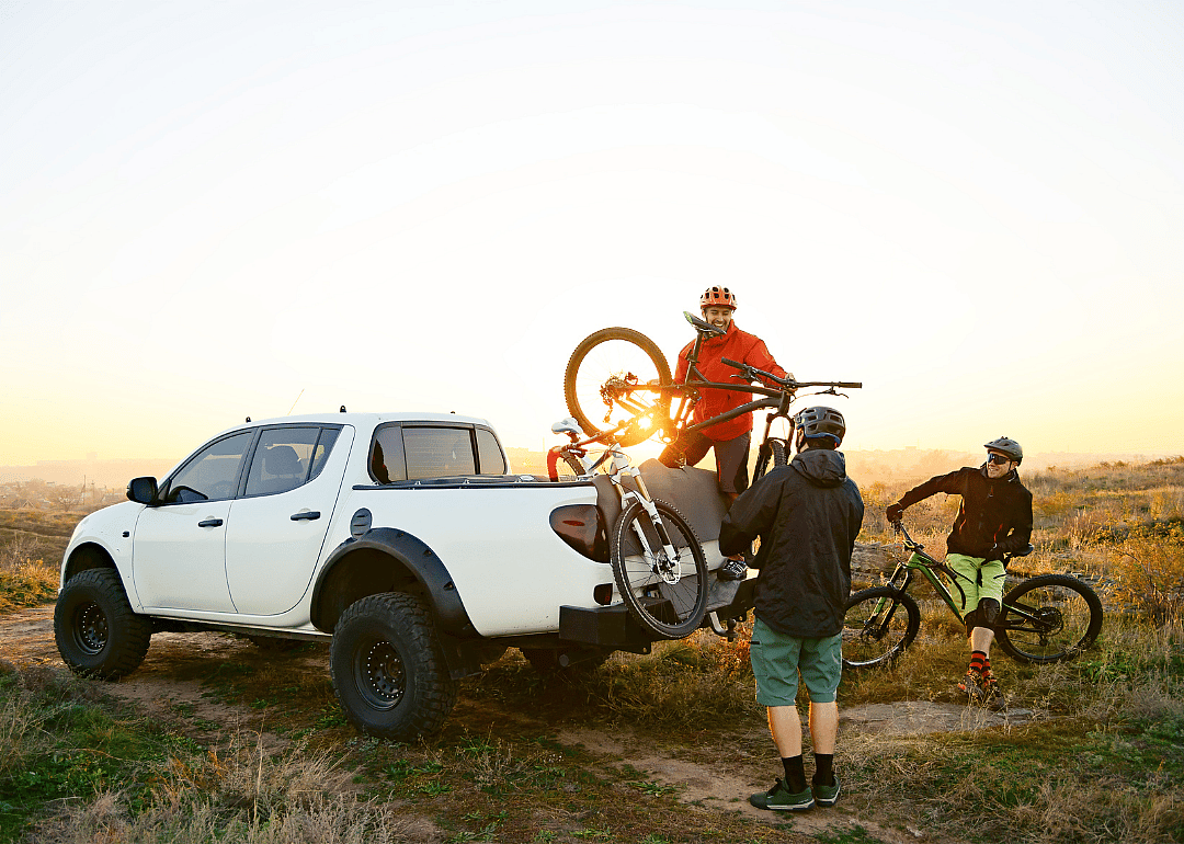 Cyclists taking their bikes out of the bed of a pickup truck.