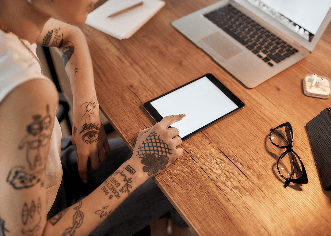 A young tattooed woman using a digital tablet while sitting at her workplace.
