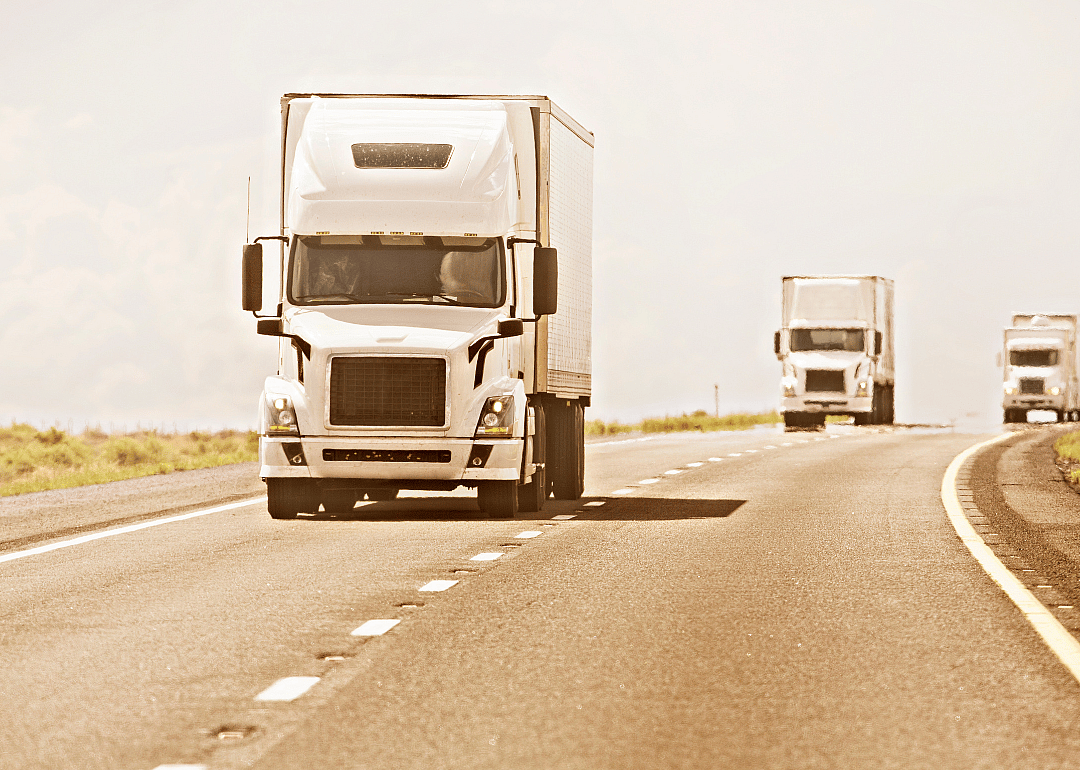 Three identical white trucks driving down a highway.