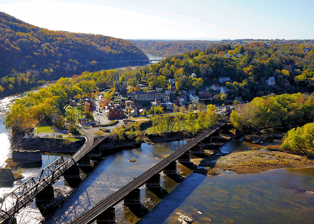 Aerial view of a town by the river surrounded by lush green trees with two bridges in the foreground.