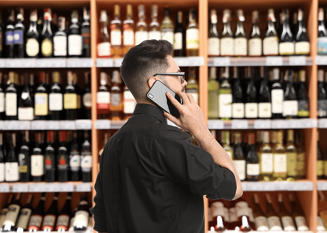 An employees speaks on the phone in front of shelves of wine in a wholesale outlet.