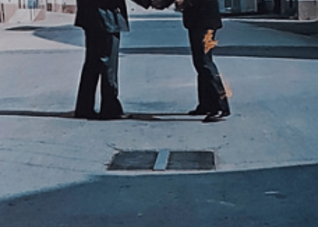 Painting of two legs—one on fire—and a grate in the street.