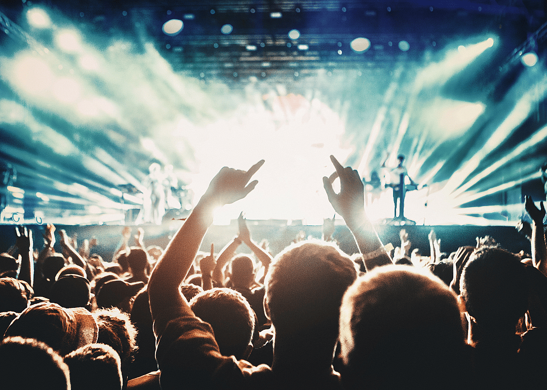Concert crowd silhouettes with brightly lit stage with a band playing in the background.
