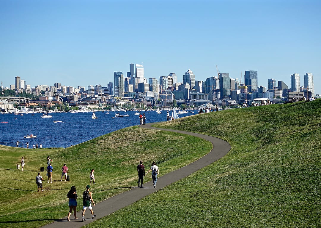 People walking in a park on the water with downtown Seattle in the background.