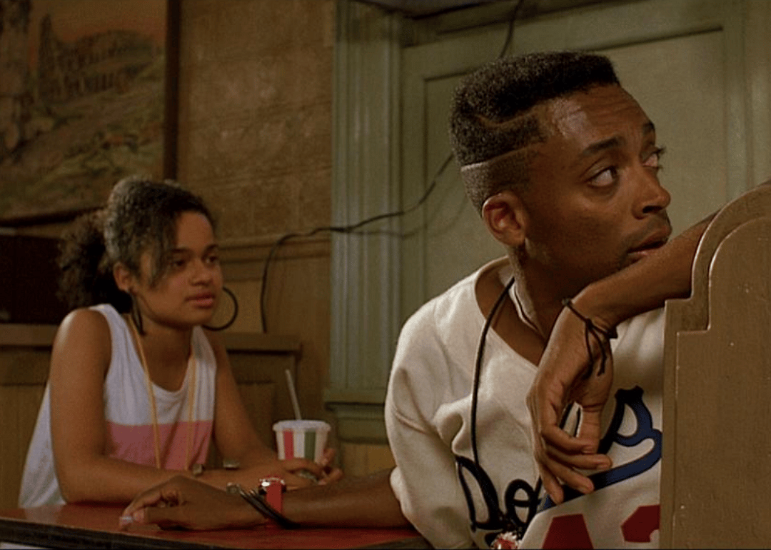 Spike Lee sitting at a booth with a woman as he looks behind his seat.