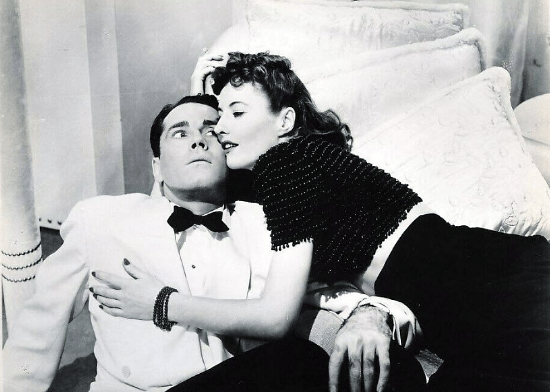 A man in a suit sitting on the floor while a woman smothers him with a hug.