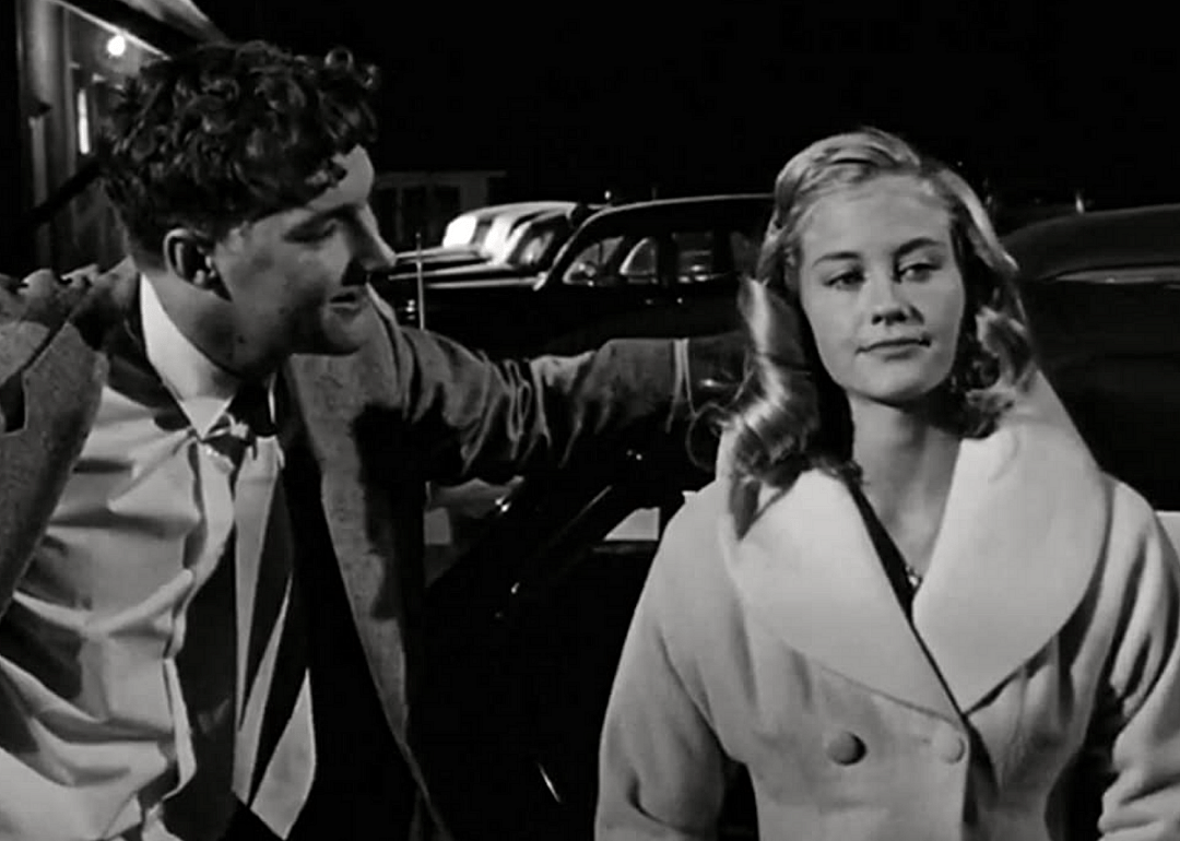 Randy Quaid and Cybill Shepherd leaning against a classic car.
