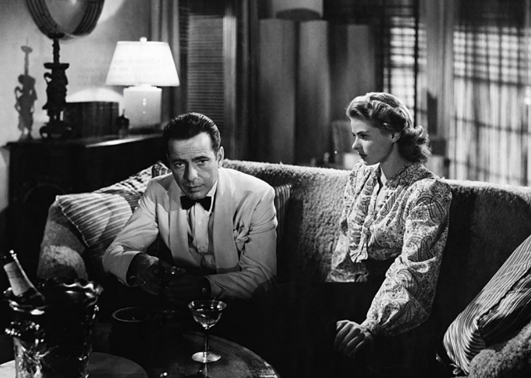 Humphrey Bogart and Ingrid Bergman sitting on a couch together with cocktail glasses.