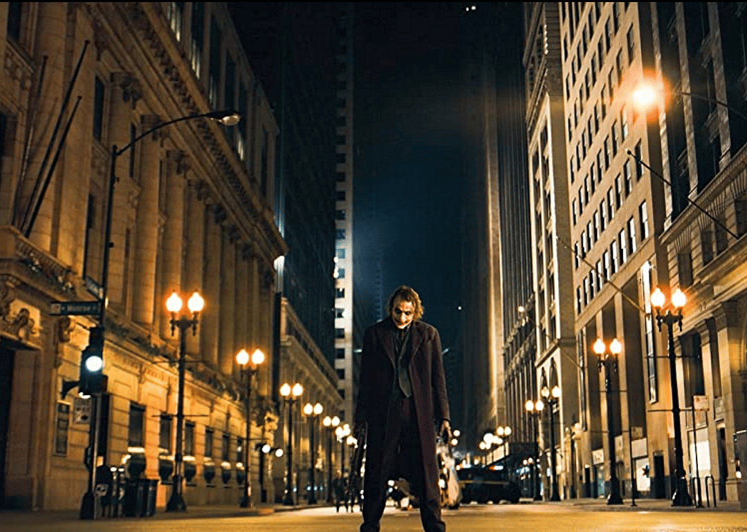 Heath Ledger dressed as the Joker in a purple suit standing in the street.