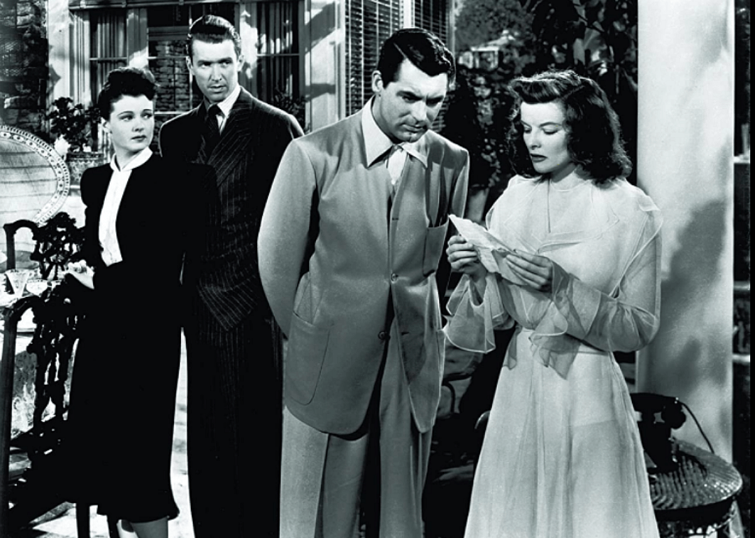 Katharine Hepburn reads a letter to Cary Grant while a man and woman look on.