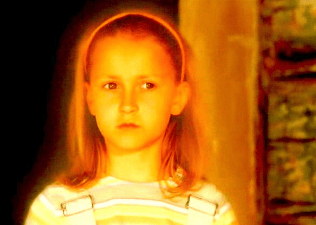 A little girl's face is glowing from what looks to be a fire she's watching.