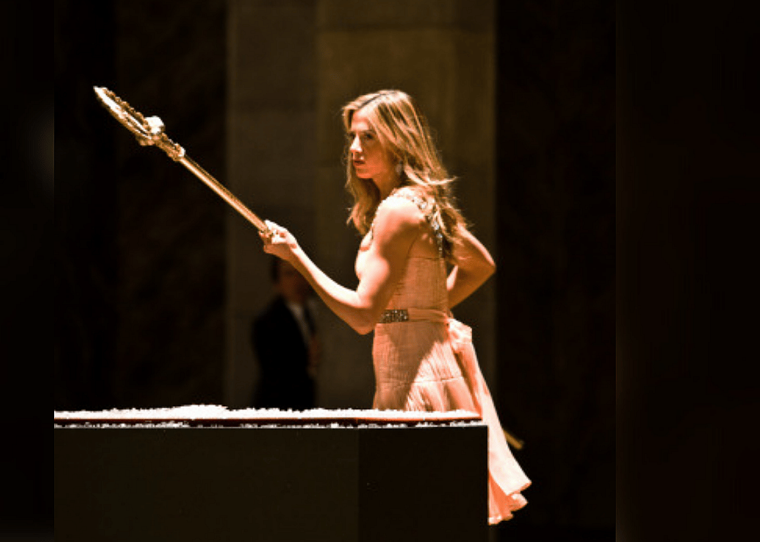 A woman in a pink dress holds a spear inside a tomb.