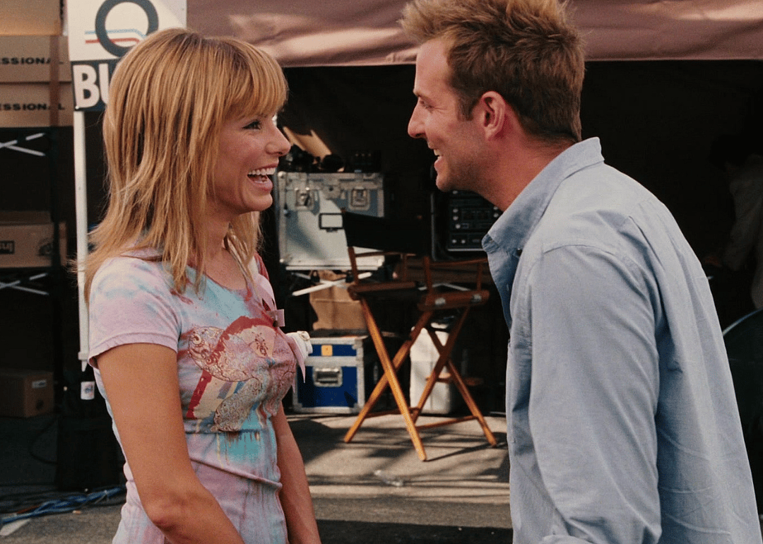 Sandra Bullock and Bradley Cooper laughing on a news set.