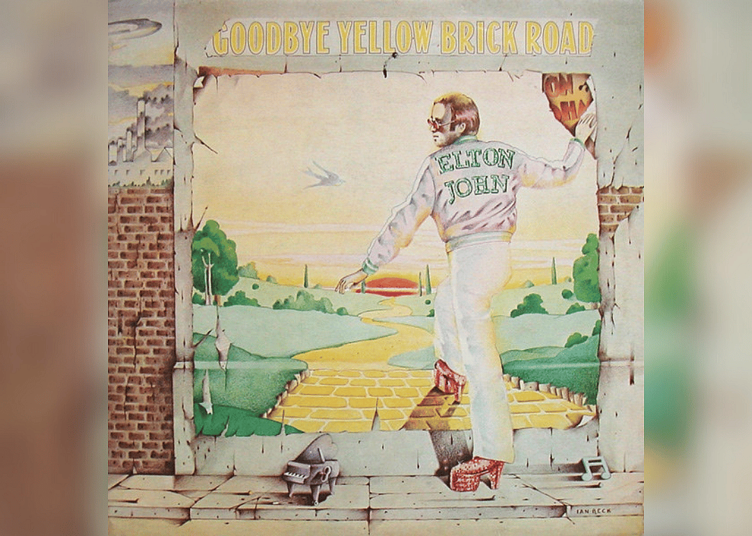 A cartoon of Elton John wearing platform ruby slippers and stepping into a brick wall where the yellow brick road begins and leads to Oz.