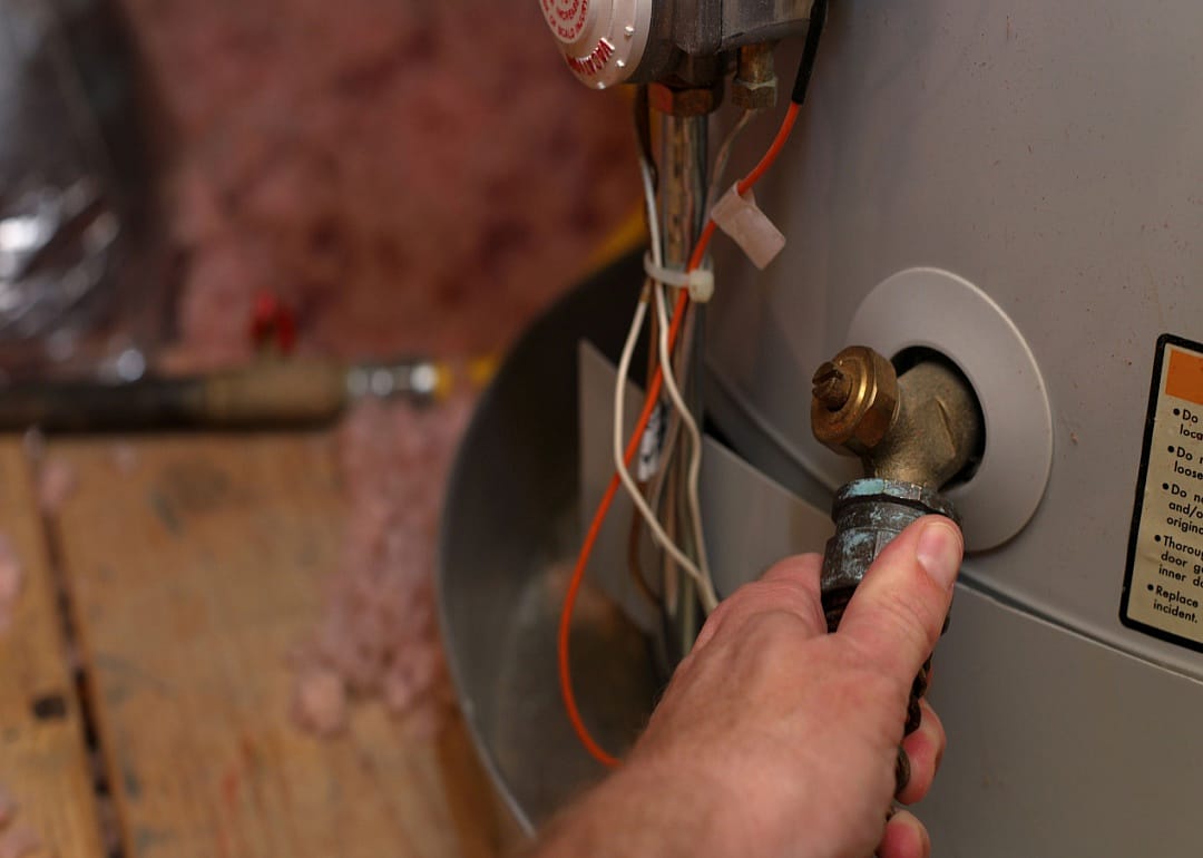 A man has his hand on a knob of a hot water heater.