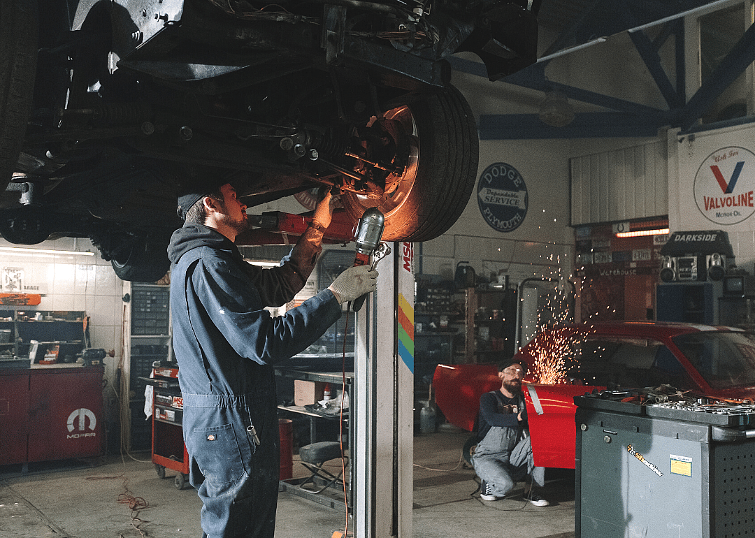Two automotive technicians working on vehicles in a shop.