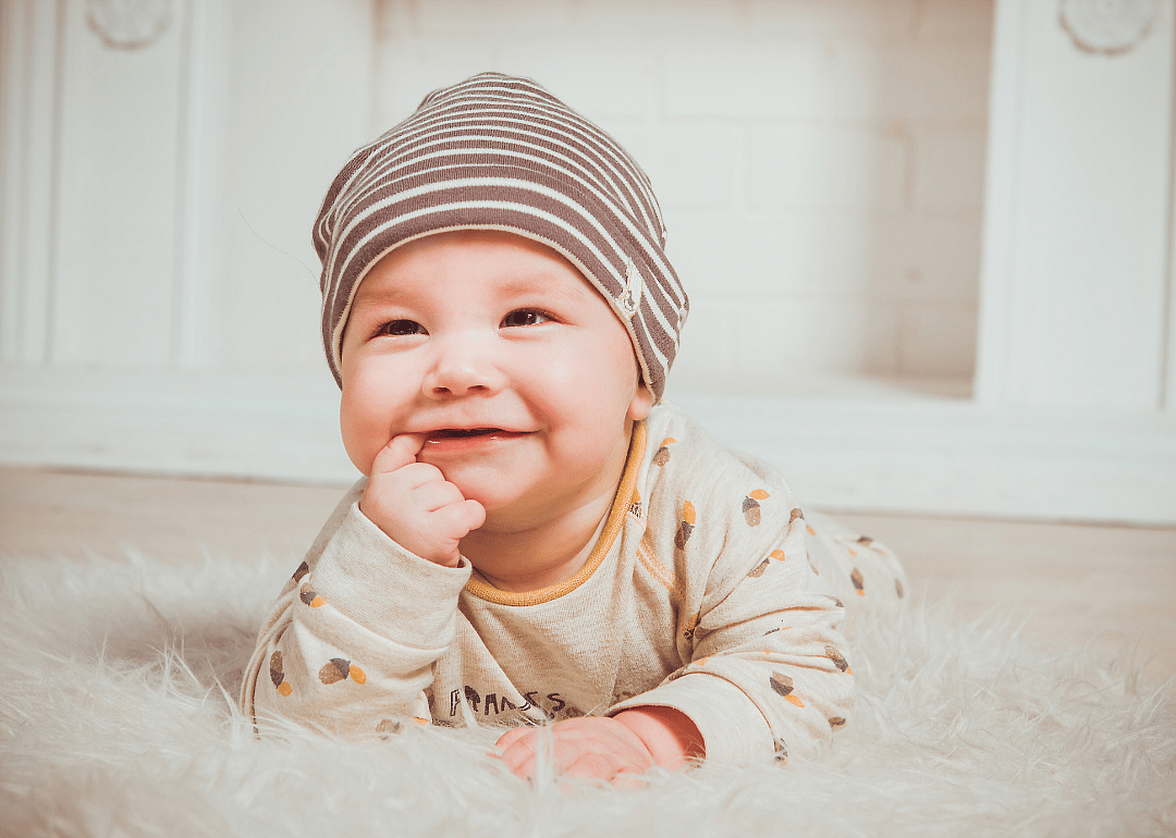A baby on a fluffy white rug with a brown hat.