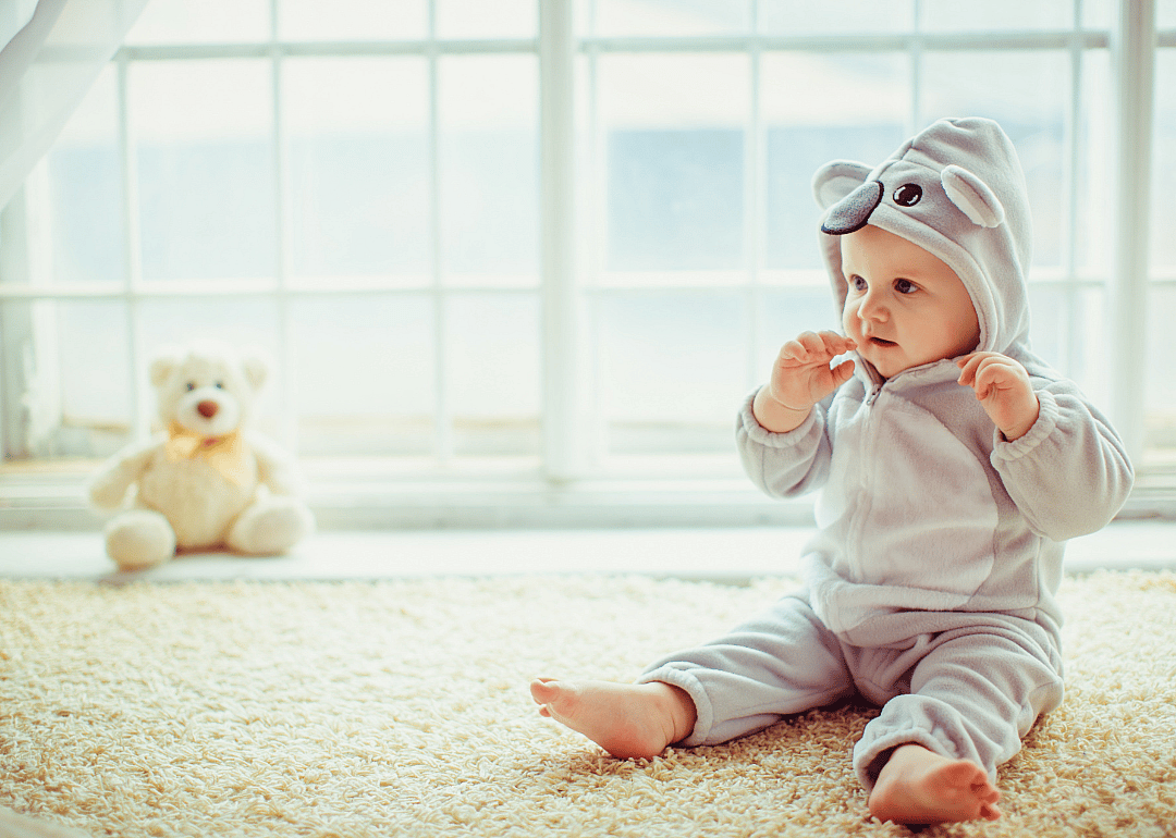 A baby sitting on carpet wearing an elephant outfit.