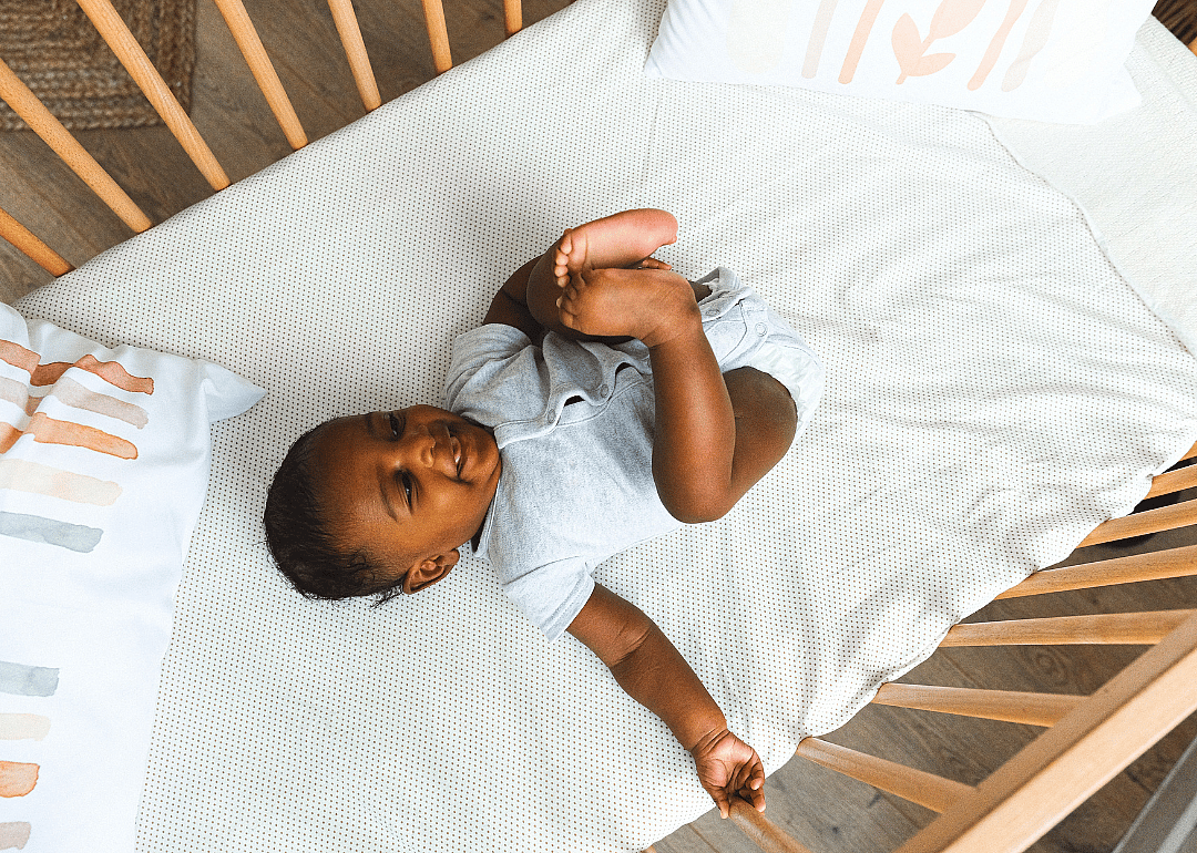 A baby in a wooden crib with pillows.