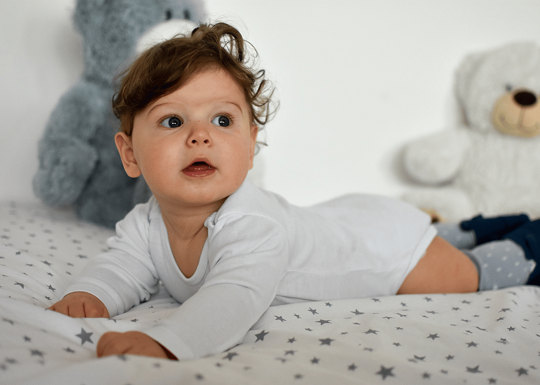 A baby wearing a white onesie on a bed with star sheets.