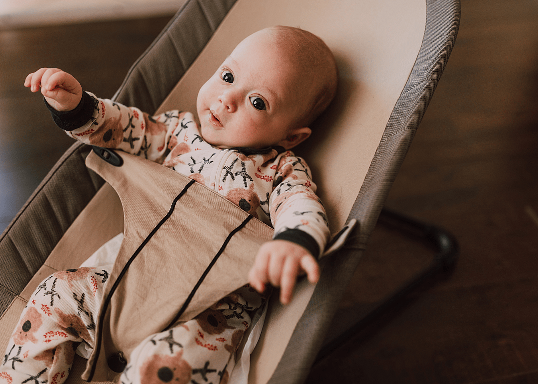 A baby in a colorful outfit in a bouncer.