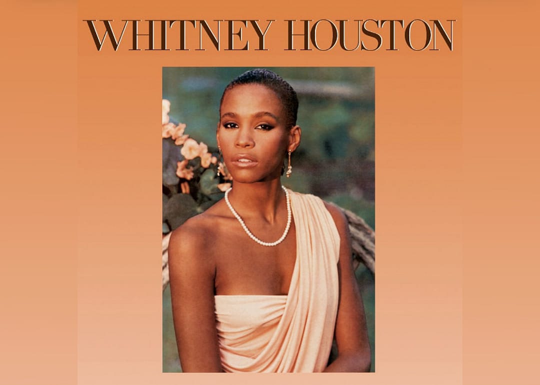 A young Whitney Houston wearing a one shoulder gown and pearls.