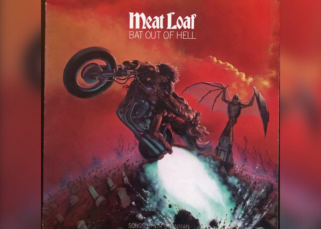 A naked man riding a motorcycle while a horse skeleton erupts from the grounds of a cemetery.
