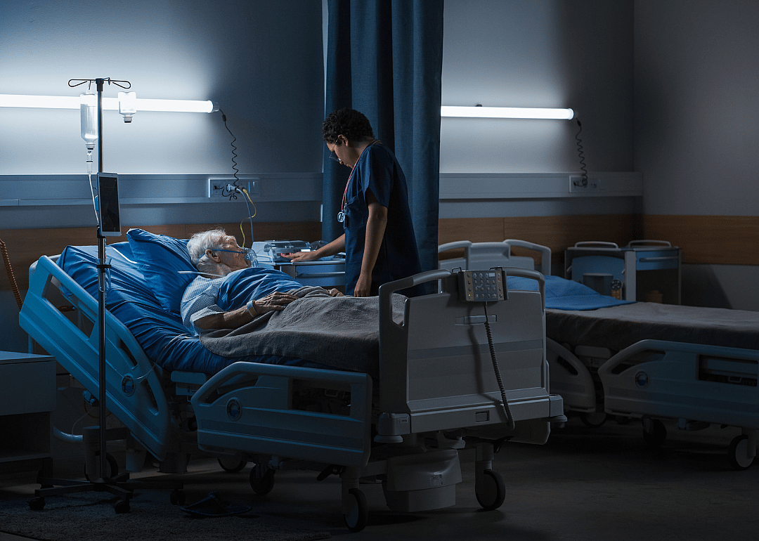 Elderly patient in hospital bed being cared for by a nurse.