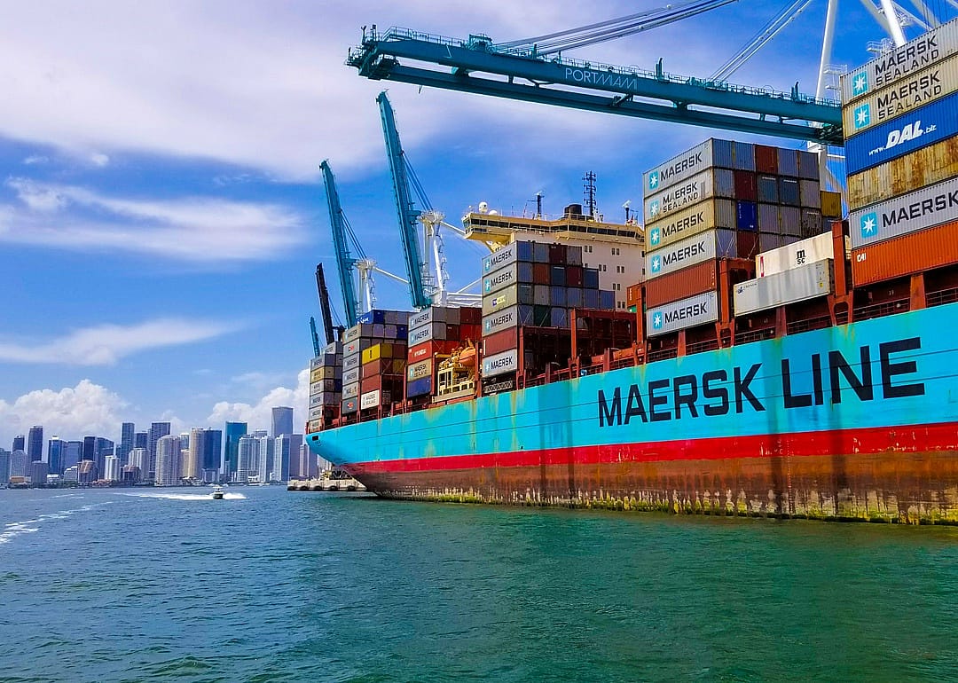 A Maersk shipping vessel loaded with containers and Miami in the background.