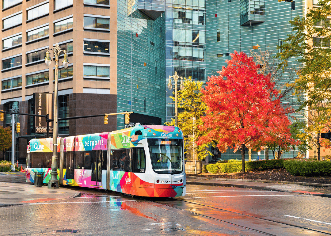 A colorful city tram in downtown with fall trees and buildings in the background.