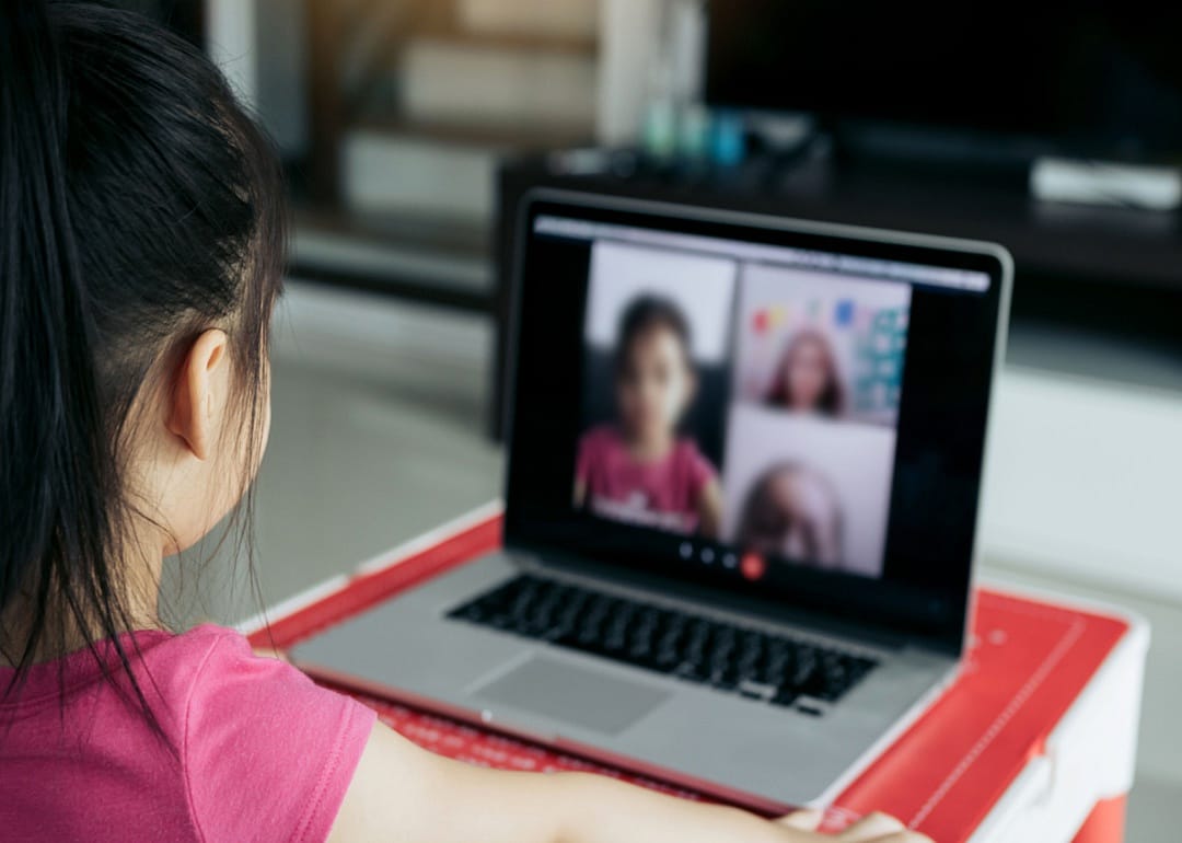 A young girl with headphones on sitting at desk doing virtual learning.