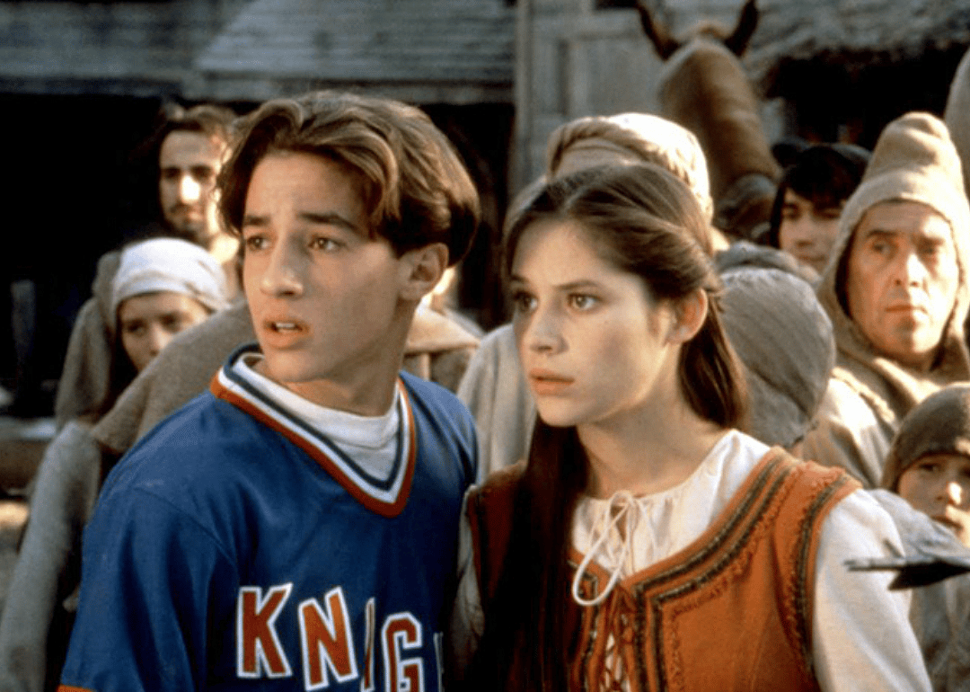 A boy in a Little League baseball uniform with a girl in medieval times dress.