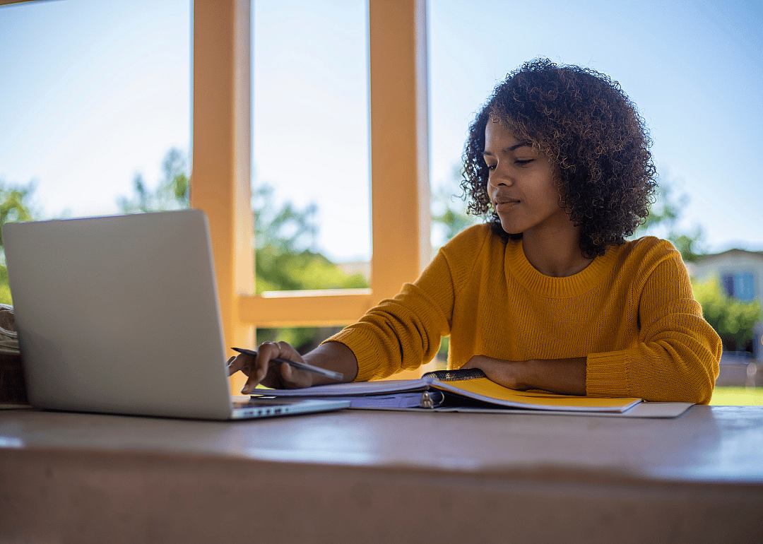 A student in an orange sweater working on a laptop.