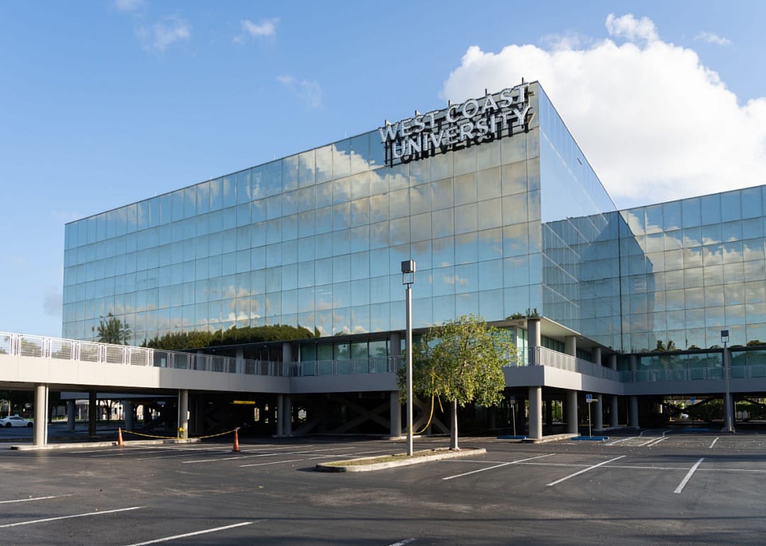 A tall reflective building bearing a West Coast University sign.