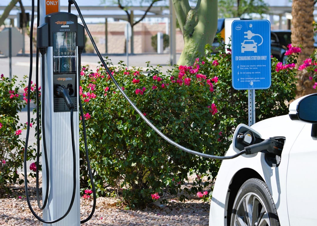 A small white car charging at a charging station at an employee parking spot.