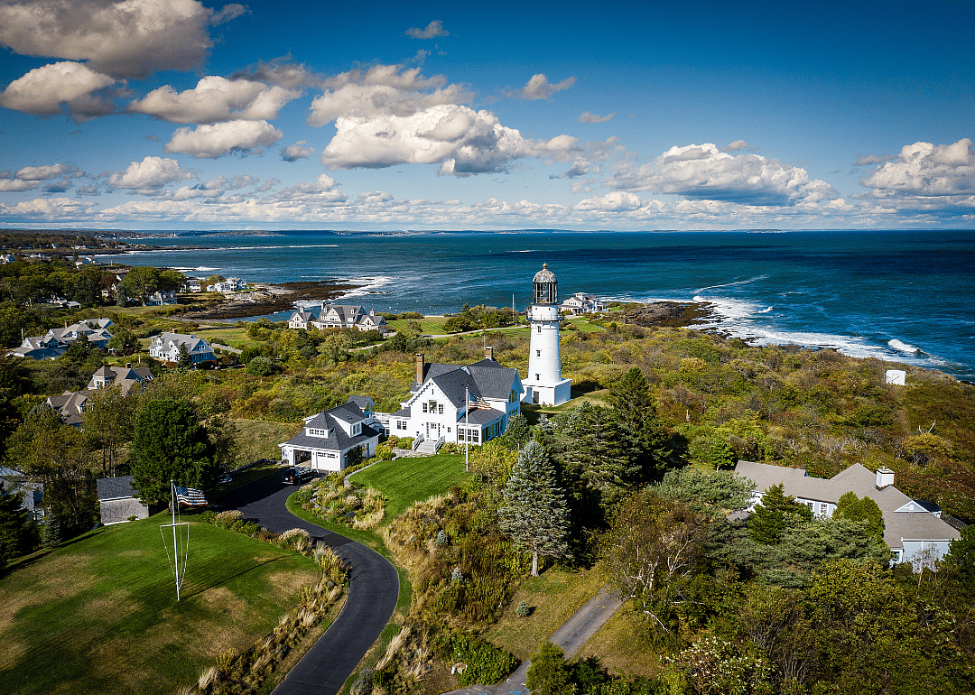An aerial view of a lighthouse and homes near the water.
