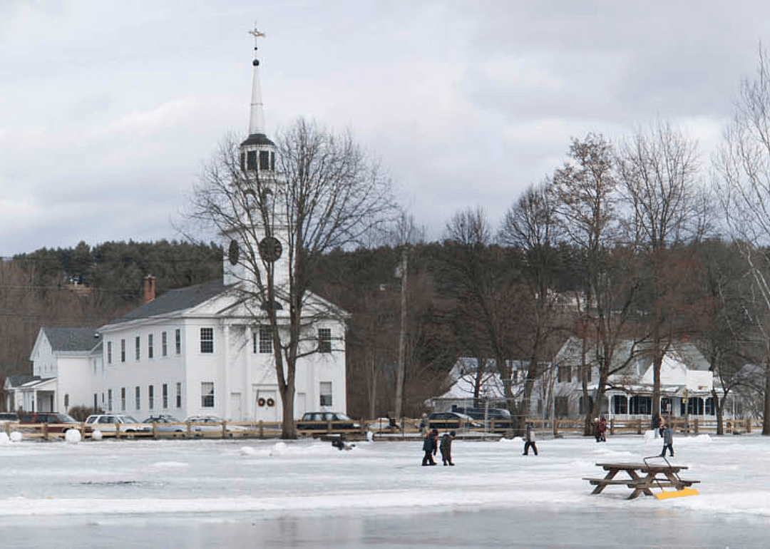 People in the snow in front of a white church and homes.
