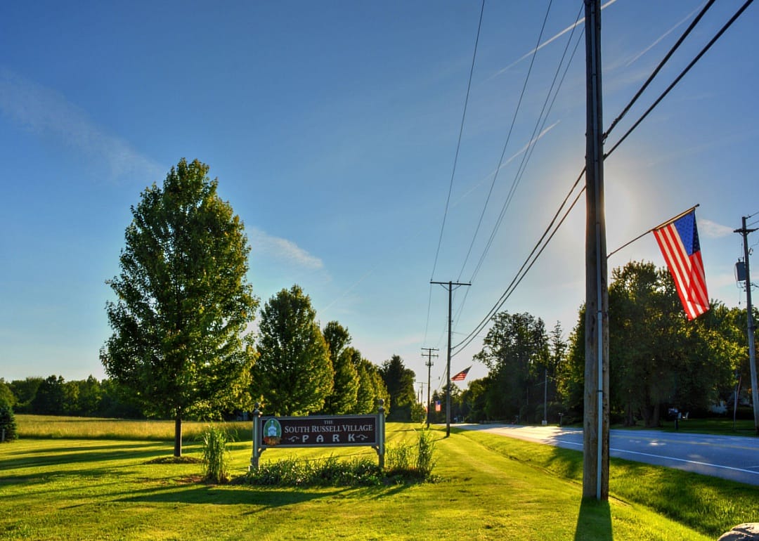 A sign for a park lined with trees and American flags.