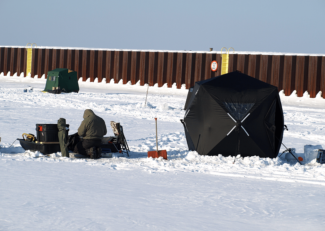 A person bundled up, surrounded by ice fishing supplies. 