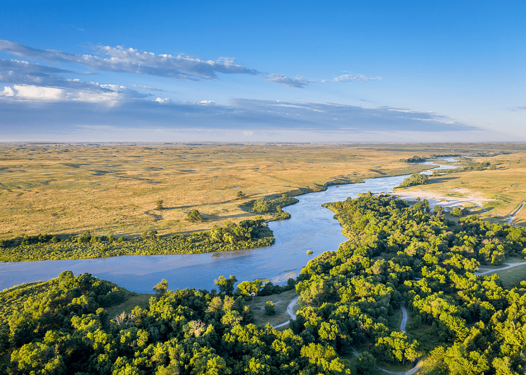 Aerial view of a small river winding through plains on one side and grass and trees on the other., 
