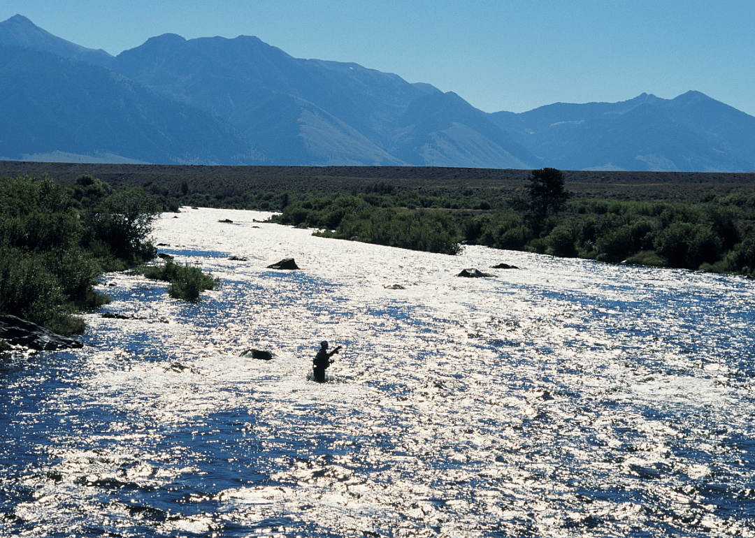 A silhouette of a person standing in waist deep water with mountains in the background. 