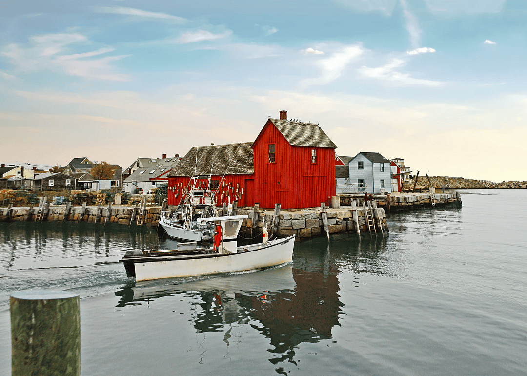 A red structure at the end of a stone boardwalk with a couple of small boats in the water. 