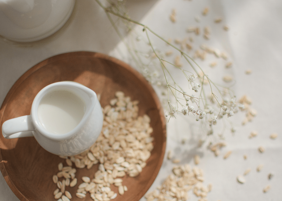 A small jar of oat milk in a wooden tray of oats.