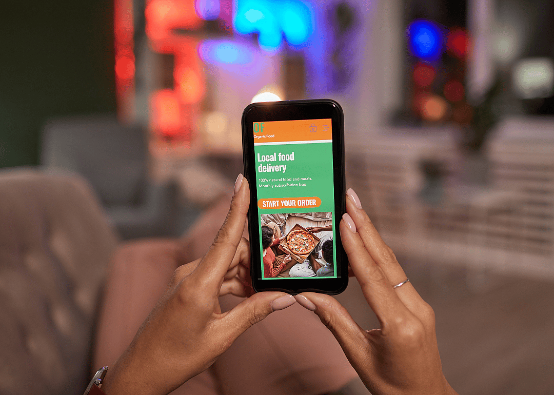 A person holding a phone with a restaurant app open to a pizza delivery.